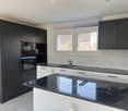 modern kitchen with black cabinets, white countertops, black granite countertop, built-in oven and microwave, sink with faucet, window