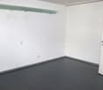 empty room with white walls, gray floor, mounted shelf, power outlets, and an open door