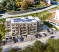 Aerial shot of a multi story building with multiple balconies, parking lot, solar panels on roof, located on the slope.