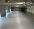 Large open warehouse space with concrete flooring, exposed ceiling beams, and overhead lighting. The space appears to be empty and ready for use.