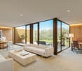 Spacious open-plan office with large windows overlooking a lush outdoor garden. The room features a comfortable seating area with a beige sofa and a wooden coffee table, as well as a work area with desks, chairs, and various decor elements. The walls are