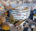 Modern office building with raised ground floor, green roofs, and surrounded by parking lots and boats