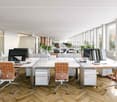 modern office with parquet flooring, white desks, brown chairs, multiple windows, large windows at the end