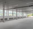 An empty office space with fluorescent ceiling lights, pillars, and windows.