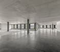 open room, large windows, gray tiled floor, concrete ceiling, doors at the end