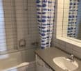 Tiled floor, white vanity with sink, mirror, shower curtain, window