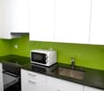 modern kitchen with green splashback, white cabinetry, black countertops, electric stove, oven, stainless steel sink, faucet, white microwave, power outlet