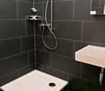 black tiles, white shower area, white sink, silver faucet, shower head, soap dish, green towel