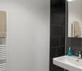 small bathroom with white sink, black tiles, white walls, towel rack, mirror, soap dispenser