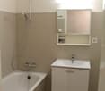 Bathtub with showerhead, white countertop, mirror with shelf, power outlet on wall