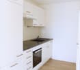 white cabinetry, wooden floors, stainless steel countertop, integrated oven, dishwasher, sink, faucet, white walls, white appliances, empty room