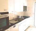 Modern kitchen with white cabinets, black countertop, built-in oven and dishwasher, tiled backsplash, and tile flooring.