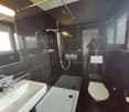 white sink, showerhead, bathtub, toilet, mirror, light fixture, black tiles