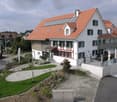 2 story house, white exterior, red roof, solar panels, green trim, large windows, raised ground floor, garden, pathway, outdoor seating