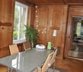 wooden wall paneling, hardwood floors, round dining table with 6 chairs, glass window, small potted plant, lamp, dark brown rug