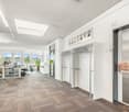Spacious open-plan office with large windows, modern furniture, and a kitchenette area with a dishwasher
