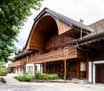 brown wooden chalet style house, large arched window, multiple windows, balcony, patio, small garden in front