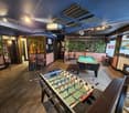 Two foosballs, a pool table, barstools, a bench, and a brick wall with a mural.