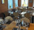 a dining area with tables and chairs, wooden walls, white curtains, wine glasses, and plates on the tables