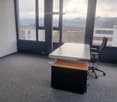Spacious office with large windows offering a scenic view, gray carpeted floor, white ceiling with recessed lighting, black office chair, and a desk with a computer monitor.