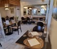 A restaurant with wooden tables and chairs, a large mirror on the wall, and a wooden ceiling with hanging lamps.