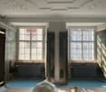 empty room, two windows, radiators, blue floor, white ceiling with decorations
