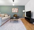 Spacious living room with gray sofa, wooden coffee table, black TV stand, hardwood floors, and abstract artwork on the wall. The room also features a floor lamp and a pendant light fixture.