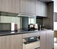 Modern kitchen with gray wood-paneled cabinets, black countertop, built-in microwave, coffee maker, and electric kettle