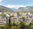 Modern residential complex with 3 buildings, solar panels, surrounded by trees, mountains in the background.