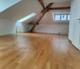Empty attic with wooden beams, hardwood floors, white walls, two attic windows, a ceiling radiator on each side of the room.