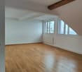 empty room, wooden floor, white walls, two windows with ocean view, white radiator, power outlet, exposed wooden beam