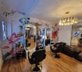Beauty salon with wooden floors, brick walls, large mirrors, seating area, and a chandelier.