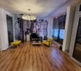 Hardwood floors, decorative chandelier, yellow armchair, black chaise lounge, glass windows, spiral staircase, white ceiling with wood texture, white wall.
