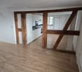 open floor plan with hardwood floors, wooden beams, white kitchen cabinets, a sink, and a window