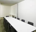 empty conference room with a long white table and black chairs, white walls, gray floor