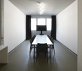 empty room, white wall, long white table, black chairs, TV, black curtains, light on ceiling