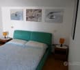 bedroom with a bed, two nightstands, and a wall with three paintings. The bed is made with two white pillows and a floral blanket. Two nightstands on either side of the bed have lamps and a power outlet each.