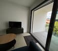 Living room: couch, wooden coffee table, black TV cabinet, flat screen TV, sliding glass door to terrace, beige tiles.