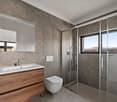 White toilet, modern sink, wooden vanity, marble tiled walls, modern shower enclosure, white and grey tiles