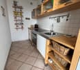 a small kitchen with tile flooring, wooden cabinets, tiled countertops, stainless steel sink and oven, and hanging shelves