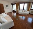 Spacious living room with white couches, glass coffee table, wooden floors, large windows, balcony with curtains, picture frame, radiator
