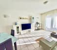 living room with white tiles, large windows, flat screen TV, coffee table, dining table, gray chairs, couch