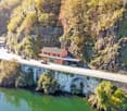 Bridge house with bridge, orange house, cars parked, trees, greenery, rocks, river