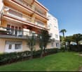 Modern apartment building with yellow walls, large balconies, and lush green gardens