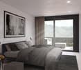 Spacious bedroom with large windows offering a scenic mountain view, dark curtains, gray bedding and decor, framed artwork on the wall, and a side table with a lamp.