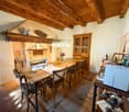 Rustic dining room with wooden beamed ceiling, wooden dining table and chairs, fireplace, shelves with decorative items, and a glass-door cabinet
