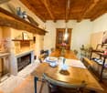 Rustic dining room with wooden beamed ceiling, wooden dining table and chairs, fireplace, shelves with decorative items, and a cabinet with glassware.