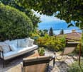 Cozy outdoor patio with a comfortable sofa, chairs, and a scenic view of the lake and mountains in the background, surrounded by lush greenery and trees