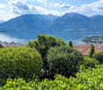 The image shows a scenic view of a mountainous landscape with a large lake in the foreground. The mountains are surrounded by lush, green vegetation, and the lake is dotted with boats and other watercraft. The city can be seen in the distance, with its bu