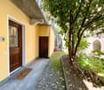 yellow wall, brown door, brick path, small garden, plants, balcony above